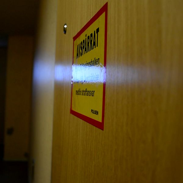 En dörr med en gul varningsskylt märkt ”Avspärrat” i en dåligt upplyst korridor. I bakgrunden syns ett avlägset rektangulärt fönster som släpper in ljus.