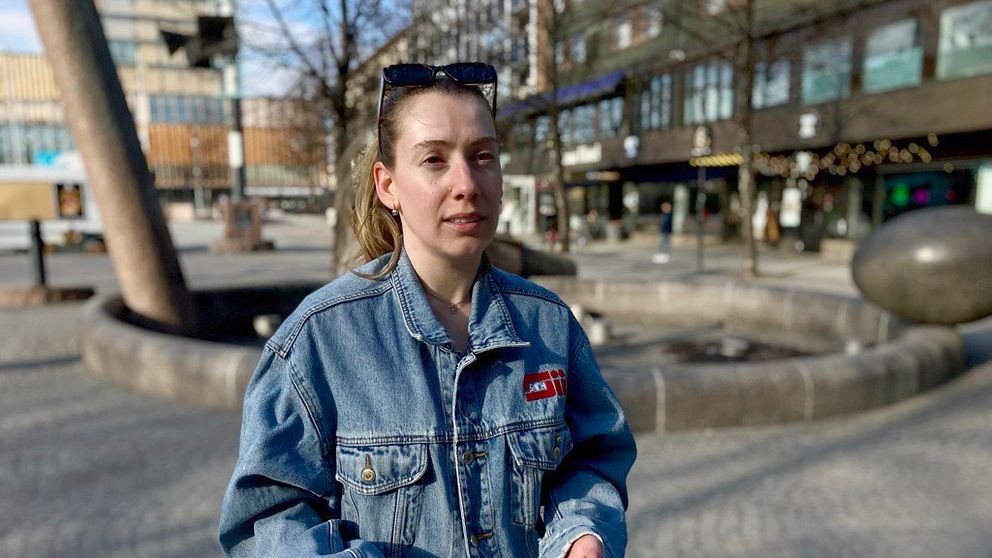 Judi Manaj i jeansjacka står vid tomt torg i Skellefteå med fontän och stadshus i bakgrunden.