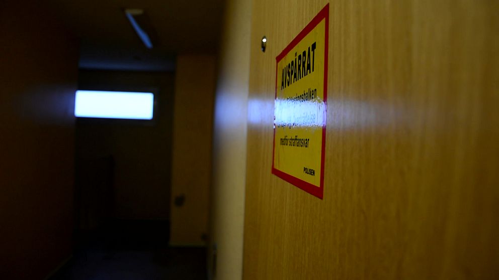 En dörr med en gul varningsskylt märkt ”Avspärrat” i en dåligt upplyst korridor. I bakgrunden syns ett avlägset rektangulärt fönster som släpper in ljus.